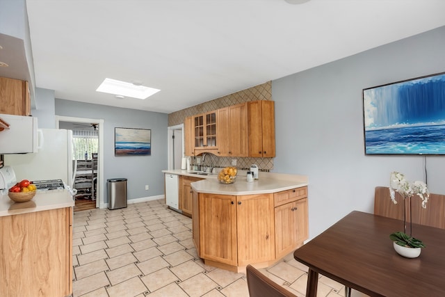 kitchen featuring a skylight, white dishwasher, light countertops, glass insert cabinets, and tasteful backsplash