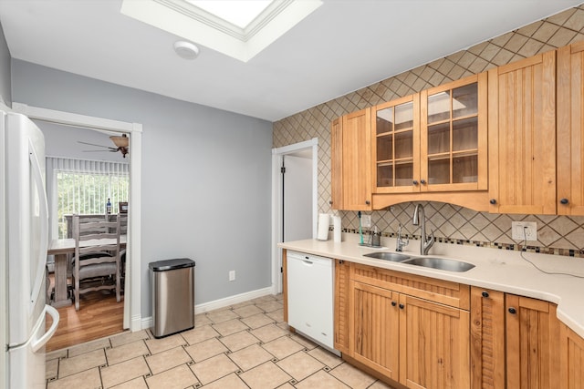 kitchen featuring baseboards, light countertops, a skylight, white appliances, and a sink