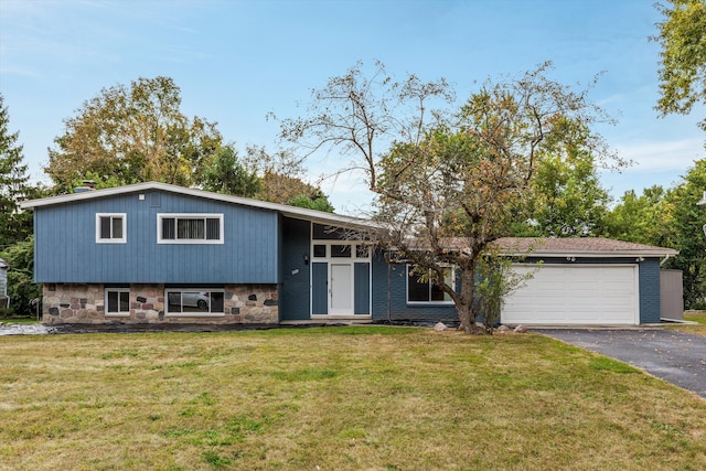 tri-level home with a front lawn, stone siding, a garage, and driveway