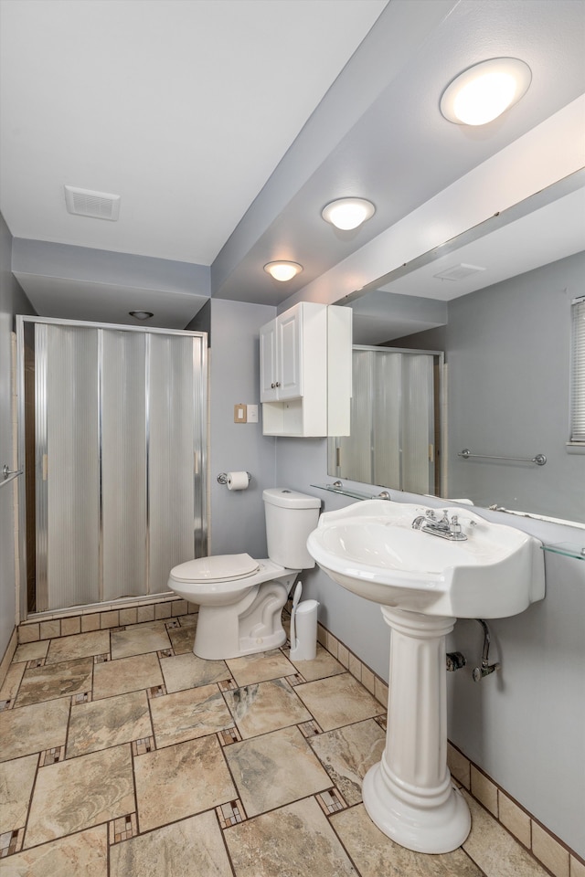 bathroom featuring visible vents, toilet, a stall shower, stone finish flooring, and baseboards