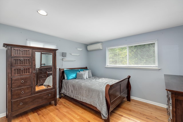 bedroom featuring a wall mounted air conditioner, baseboards, and light wood-style flooring