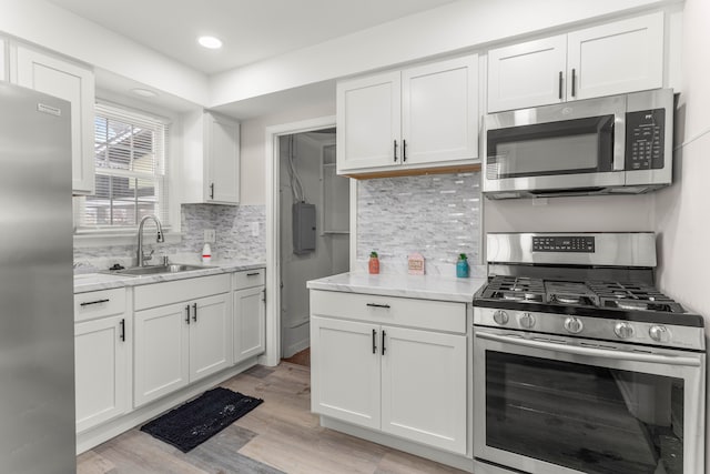 kitchen with light wood-style flooring, a sink, stainless steel appliances, white cabinets, and decorative backsplash