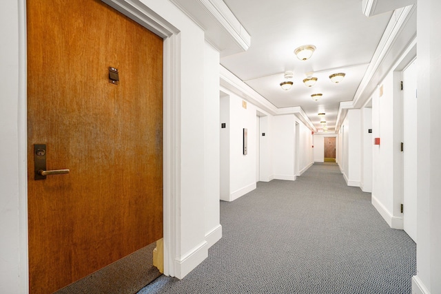 hall with ornamental molding, baseboards, and dark colored carpet