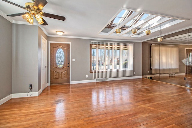 foyer entrance with wood finished floors, baseboards, visible vents, a skylight, and ornamental molding