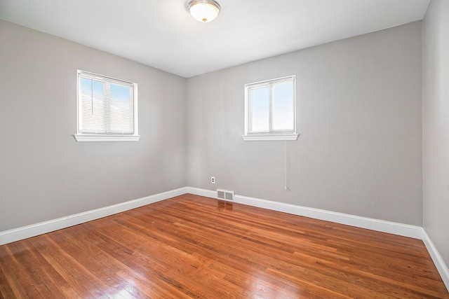 spare room featuring visible vents, a healthy amount of sunlight, baseboards, and hardwood / wood-style flooring