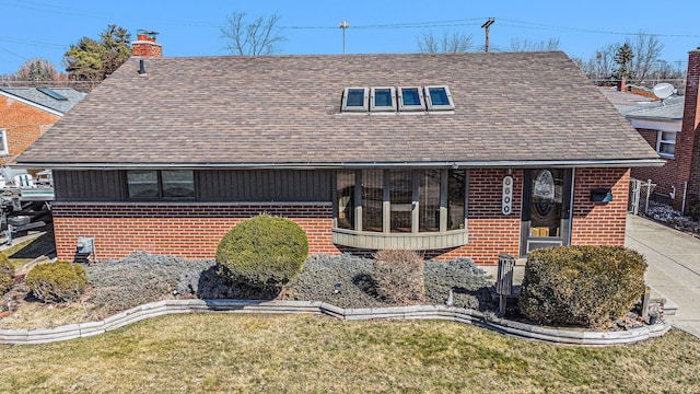 view of front of home featuring a front yard, brick siding, roof with shingles, and a chimney