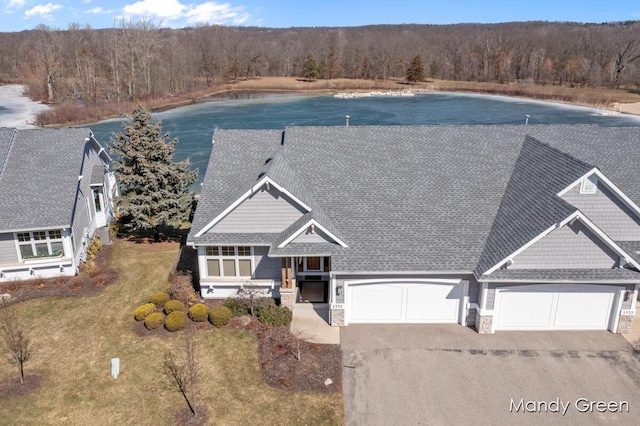 exterior space with a wooded view, a shingled roof, an attached garage, stone siding, and driveway