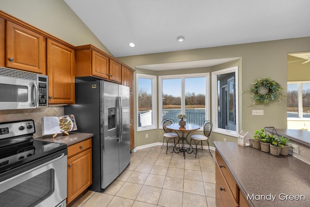 kitchen featuring dark countertops, decorative backsplash, brown cabinets, appliances with stainless steel finishes, and light tile patterned flooring