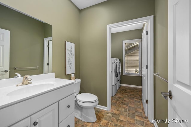 bathroom featuring vanity, baseboards, washing machine and clothes dryer, stone finish flooring, and toilet