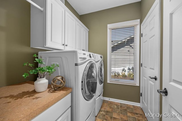 clothes washing area with stone finish flooring, cabinet space, baseboards, and washer and clothes dryer