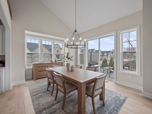 dining area featuring baseboards, high vaulted ceiling, light wood-type flooring, and an inviting chandelier