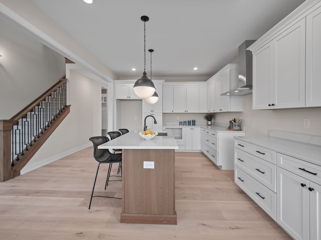 kitchen with a breakfast bar area, light wood finished floors, recessed lighting, a sink, and wall chimney exhaust hood