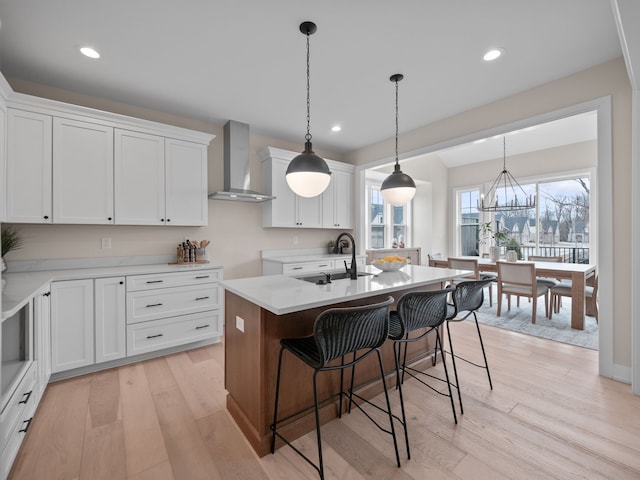 kitchen featuring light wood-style flooring, wall chimney exhaust hood, an island with sink, and a sink