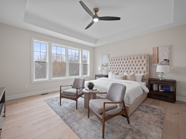 bedroom featuring visible vents, light wood-style flooring, a raised ceiling, and baseboards