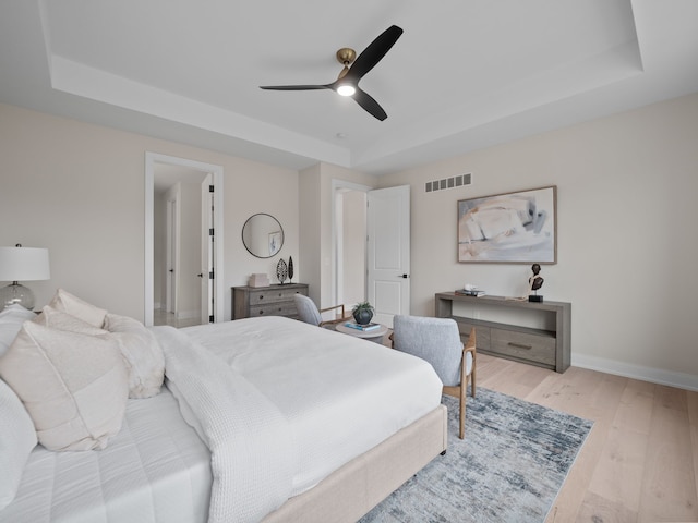 bedroom featuring a ceiling fan, wood finished floors, visible vents, baseboards, and a raised ceiling