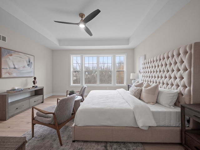 bedroom featuring a ceiling fan, wood finished floors, visible vents, baseboards, and a raised ceiling