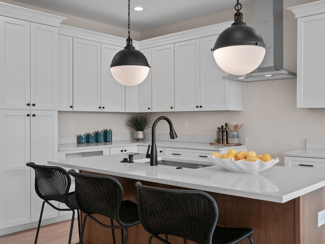 kitchen with light countertops, white cabinets, pendant lighting, a kitchen bar, and wall chimney range hood