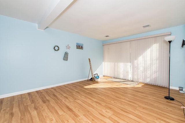 spare room with beamed ceiling, baseboards, and wood finished floors