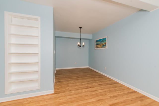 unfurnished dining area featuring an inviting chandelier, built in shelves, baseboards, and light wood finished floors