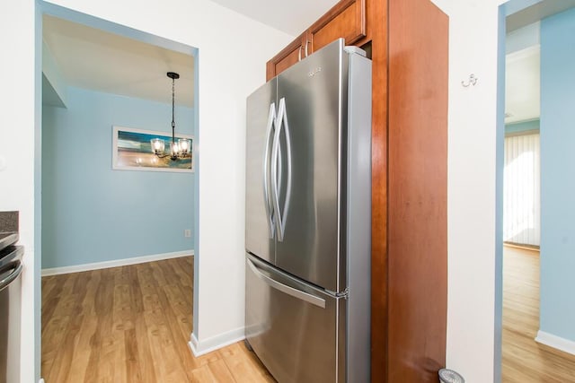 kitchen with baseboards, freestanding refrigerator, light wood-style floors, a notable chandelier, and brown cabinets