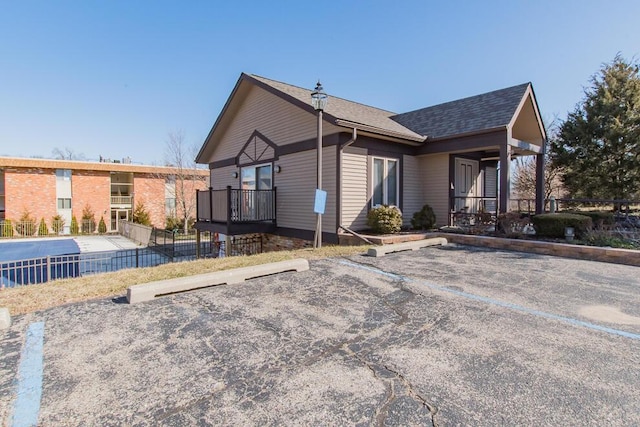 view of front of home with roof with shingles, uncovered parking, and fence