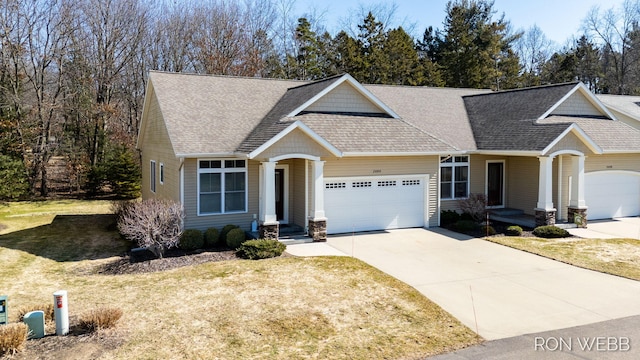 craftsman-style home featuring concrete driveway, an attached garage, a front lawn, and roof with shingles