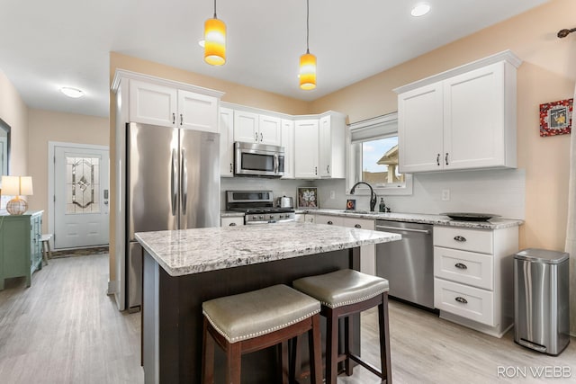 kitchen featuring light stone countertops, a kitchen island, light wood-style flooring, white cabinets, and appliances with stainless steel finishes