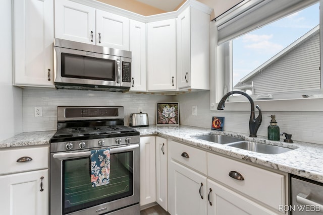 kitchen featuring light stone counters, a sink, stainless steel appliances, white cabinets, and backsplash