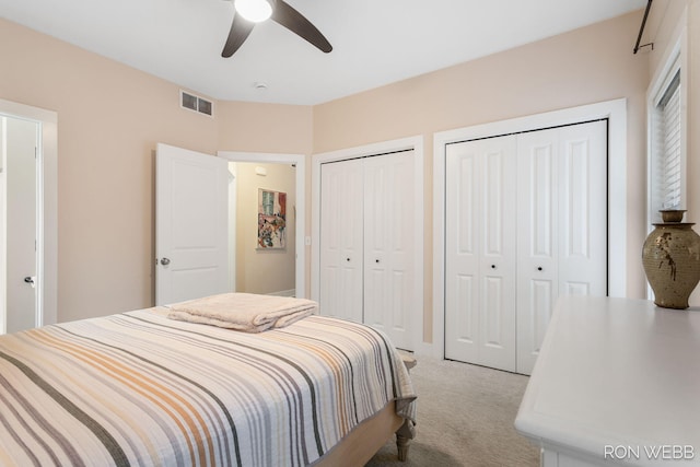 bedroom featuring ceiling fan, light colored carpet, visible vents, and multiple closets