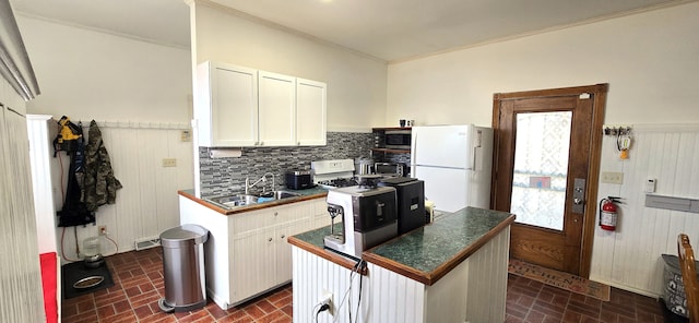 kitchen featuring a sink, stainless steel microwave, dark countertops, freestanding refrigerator, and brick floor