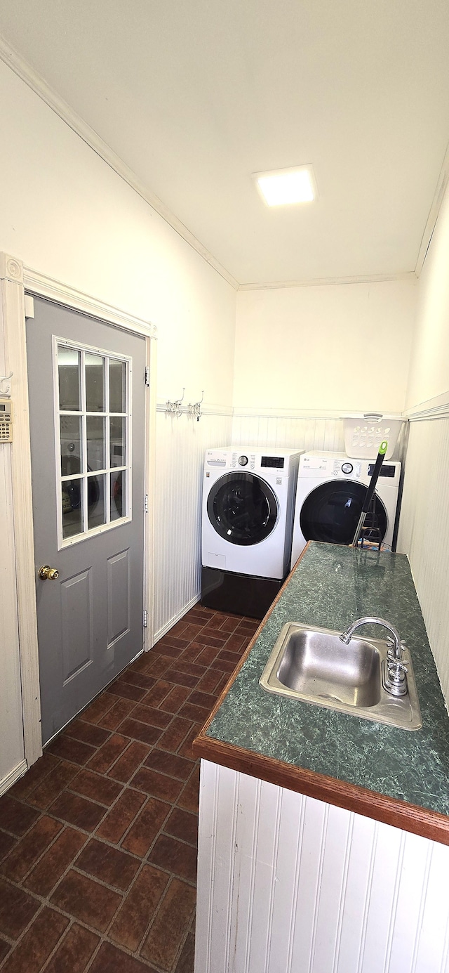 clothes washing area featuring ornamental molding, washer and clothes dryer, a sink, brick floor, and laundry area