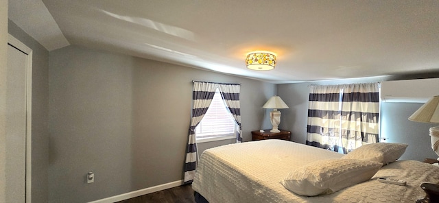 bedroom featuring dark wood finished floors, lofted ceiling, a wall unit AC, and baseboards