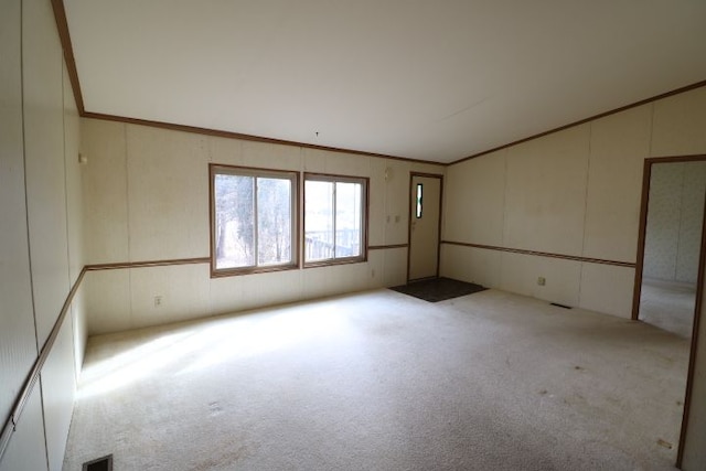 carpeted empty room featuring crown molding, a decorative wall, visible vents, and vaulted ceiling