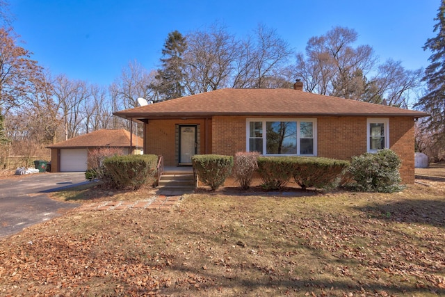 single story home featuring a porch, a chimney, an outdoor structure, a detached garage, and brick siding