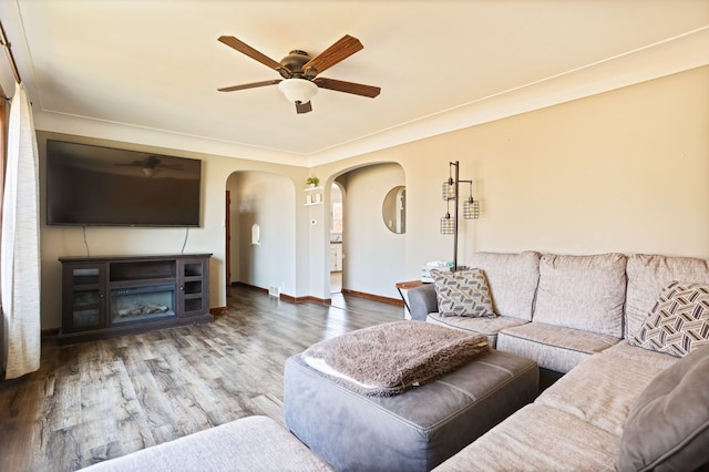 living area with baseboards, ceiling fan, wood finished floors, arched walkways, and a glass covered fireplace