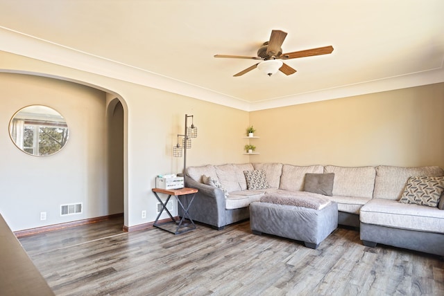 living room with a ceiling fan, wood finished floors, visible vents, baseboards, and arched walkways