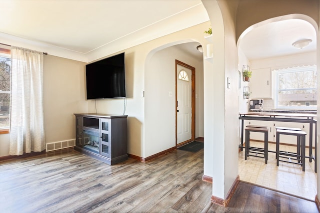 living room featuring visible vents, arched walkways, plenty of natural light, and wood finished floors