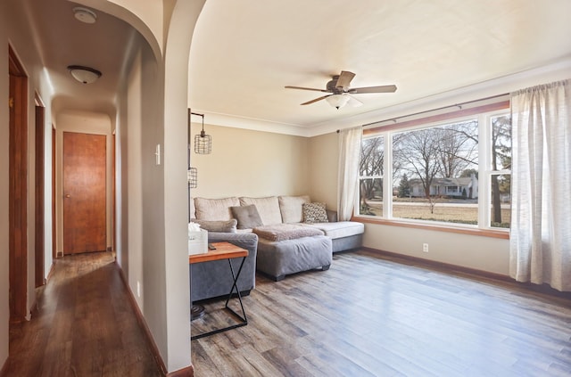 living room with a ceiling fan, wood finished floors, arched walkways, and baseboards