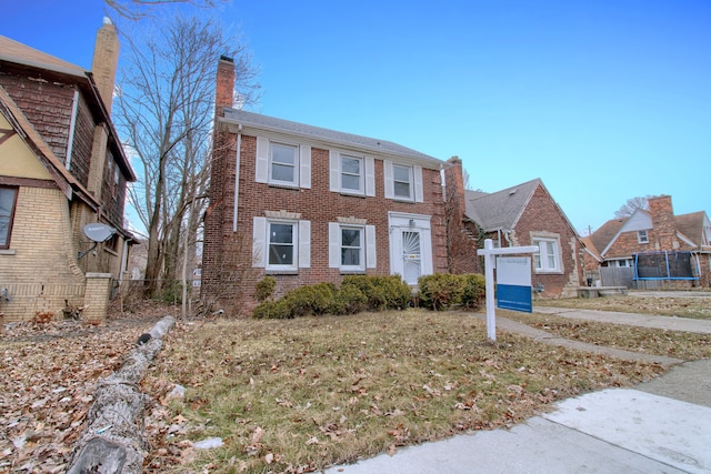 view of front of home featuring brick siding, a trampoline, and a chimney