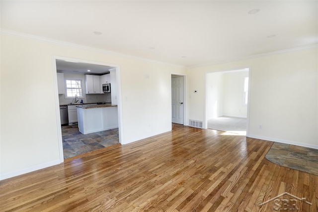 unfurnished living room featuring crown molding, wood finished floors, visible vents, and baseboards