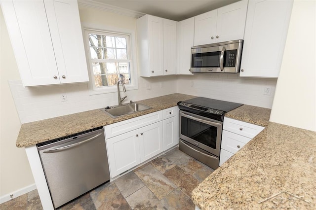 kitchen featuring a sink, decorative backsplash, white cabinets, stone finish floor, and appliances with stainless steel finishes