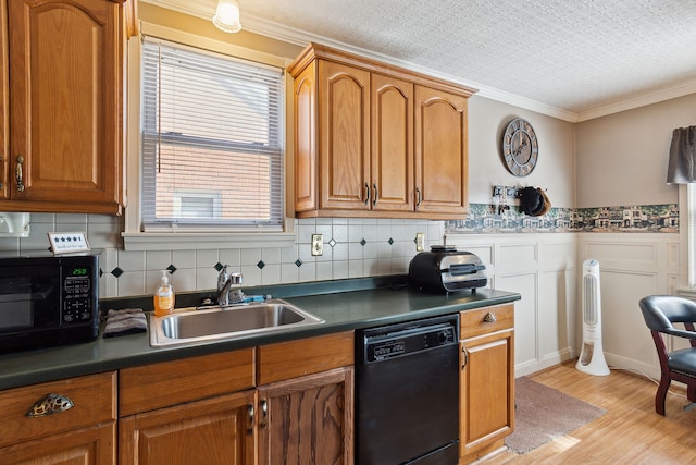 kitchen featuring dark countertops, ornamental molding, wainscoting, black appliances, and a sink