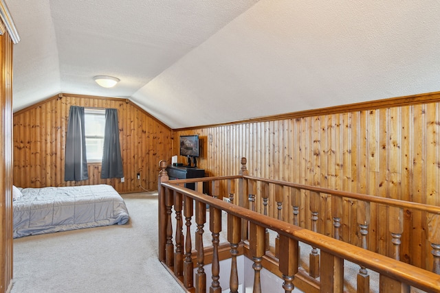 bedroom featuring wooden walls, lofted ceiling, a textured ceiling, and carpet flooring