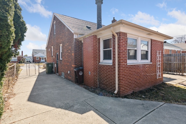 view of side of home featuring brick siding, a gate, and fence