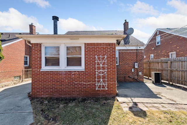 rear view of house with cooling unit, fence, a chimney, a patio area, and brick siding