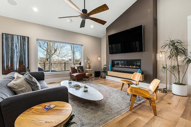 living room with baseboards, wood finished floors, a glass covered fireplace, and a ceiling fan