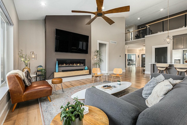 living room featuring a glass covered fireplace, wood finished floors, visible vents, and a towering ceiling