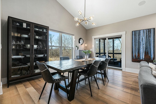 dining room with baseboards, high vaulted ceiling, an inviting chandelier, and wood finished floors