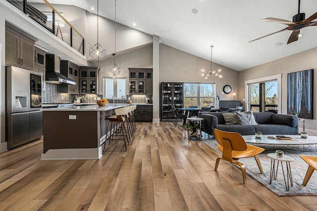 kitchen featuring wood finished floors, a kitchen island, stainless steel fridge with ice dispenser, dark brown cabinets, and wall chimney exhaust hood