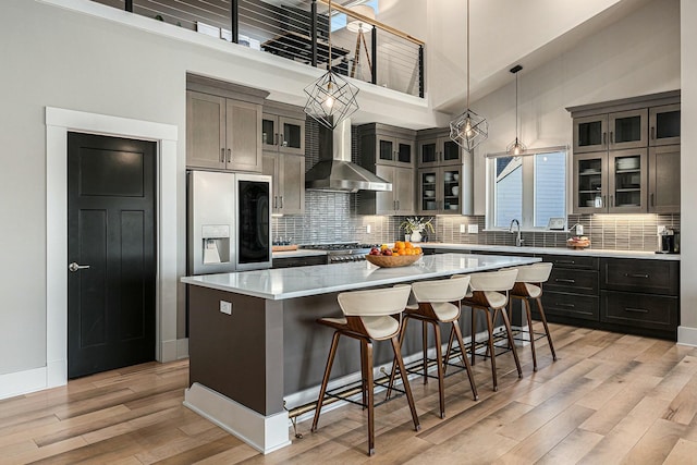 kitchen featuring stove, a towering ceiling, fridge with ice dispenser, wall chimney exhaust hood, and a center island